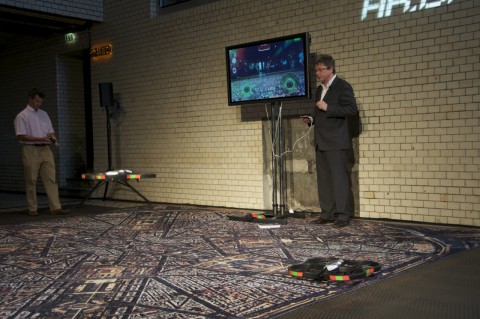 Im Hintergrund ist das Kamerabild der Drohne auf dem Fernseher zu sehen.