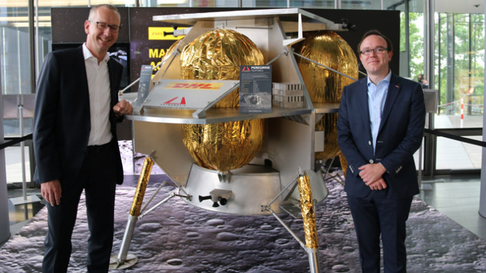Arjan Sissing (DHL Markenchef, links) und Dan Hendrickson (Vice President of Business Development bei Astrobotic, rechts) vor einem Modell des Peregrine Luna Lander (Bild: DHL, Astrobotic).